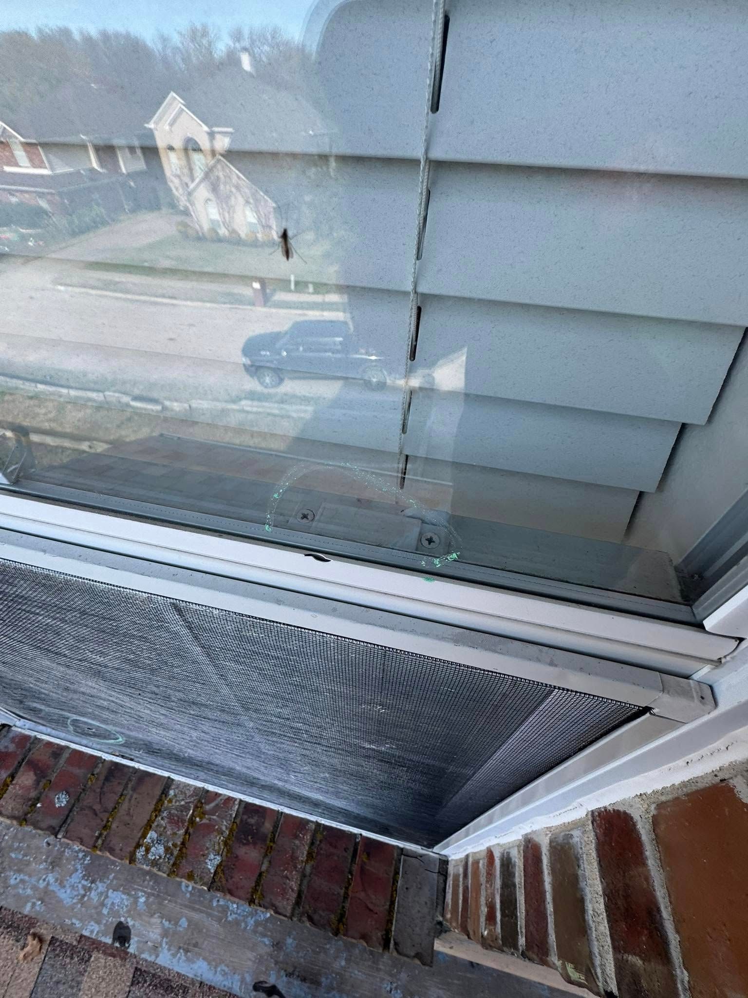 Close-up of a broken window pane above a brick patio, with spiderweb cracking and reflections on the glass