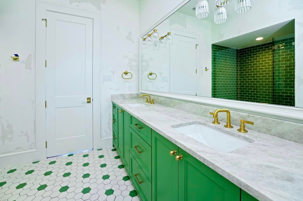 Bright bathroom with green cabinets, white marble counters, gold fixtures, and patterned green-and-white tile floor