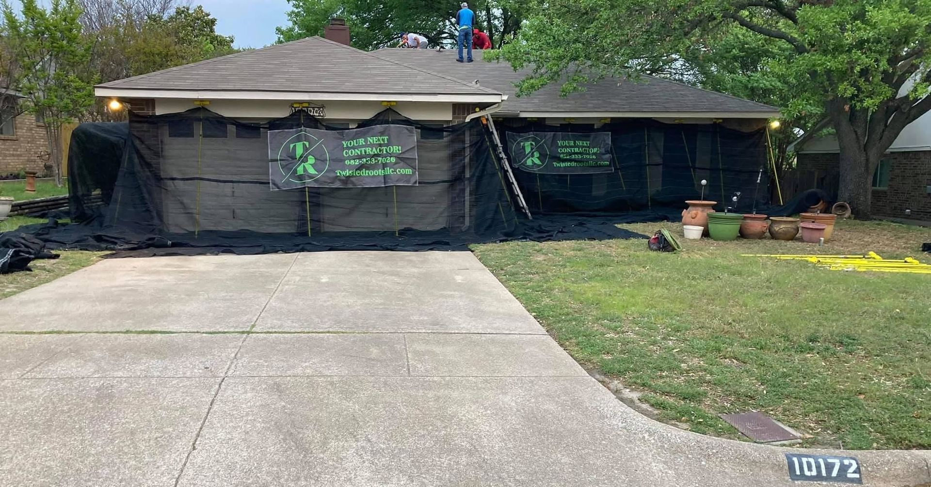 Single-story house with black tarp-covered front, concrete driveway, lawn, and a visible house number 10172