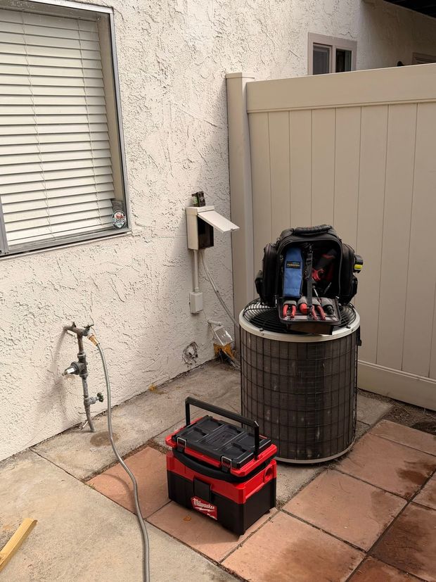 Patio with a red toolbox, open equipment on a round barrel, and a wall-mounted faucet beside a window