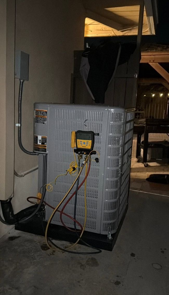 Outdoor HVAC unit with exposed yellow electrical panel and hanging wires beside a building wall