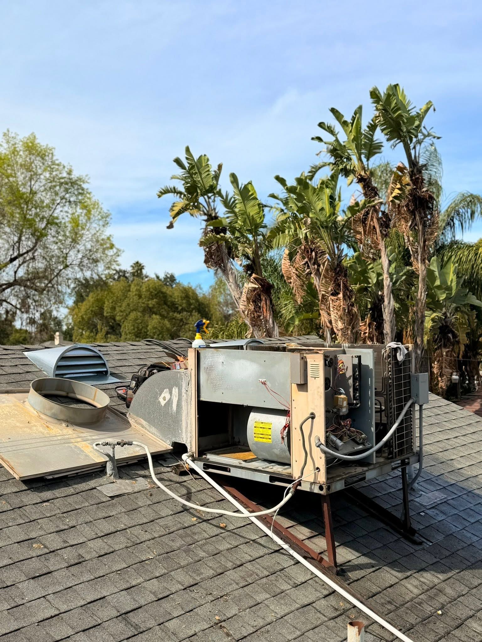 Roof-mounted HVAC unit on a sloped shingle roof with trees and a parked car in the background