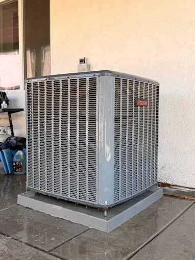 Outdoor air conditioner unit on a concrete pad beside a stucco wall.