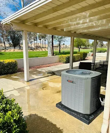 Covered patio with a gray outdoor HVAC unit beside a wet concrete floor and green lawn beyond.