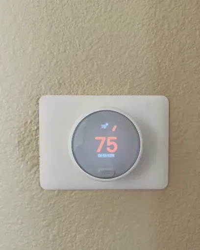 Round smart thermostat on beige wall, displaying 75° in orange.