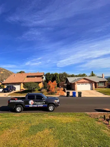 Black utility truck parked on a suburban street in front of tan houses under a blue sky.