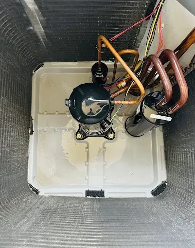 Small HVAC compressor and copper coils inside a white insulated housing box.