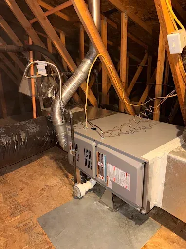 Attic HVAC unit with silver ductwork and exposed wooden rafters