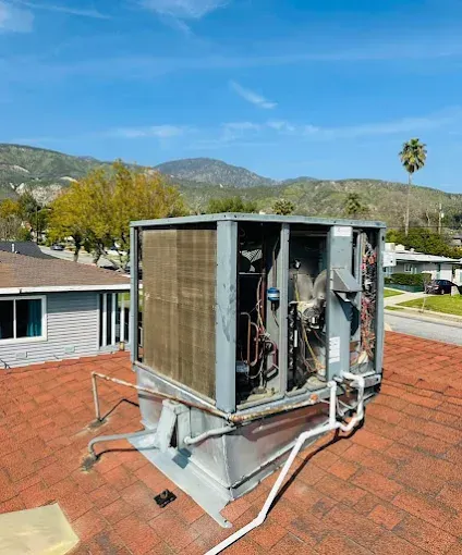 Open rooftop HVAC unit with exposed components on a red shingle roof, mountains in background