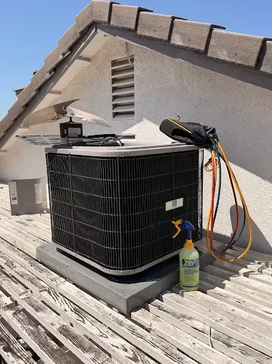 Roof-mounted air conditioner with hoses and cleaning supplies on a shingled rooftop