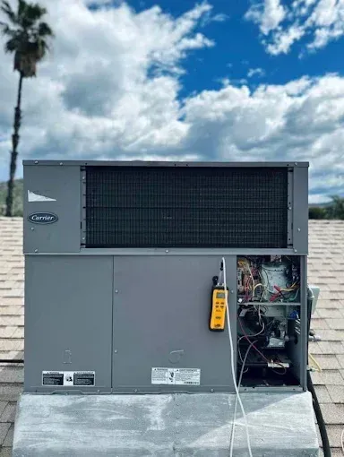 Large gray rooftop HVAC unit with open side panel and hanging yellow tag under a cloudy sky