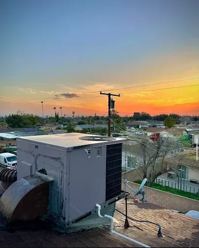 Rooftop HVAC unit at sunset with orange sky and power lines in the background