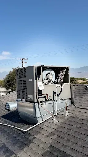 Solar rooftop HVAC unit on shingled roof under a clear blue sky.