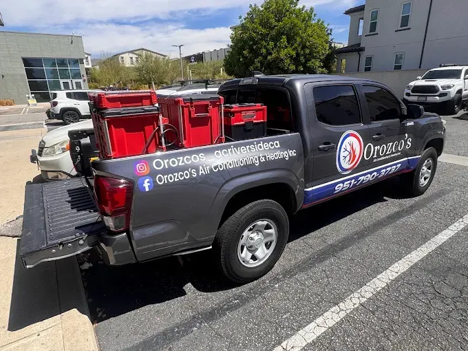 Dark gray pickup truck with red company signage parked in a lot on a sunny day
