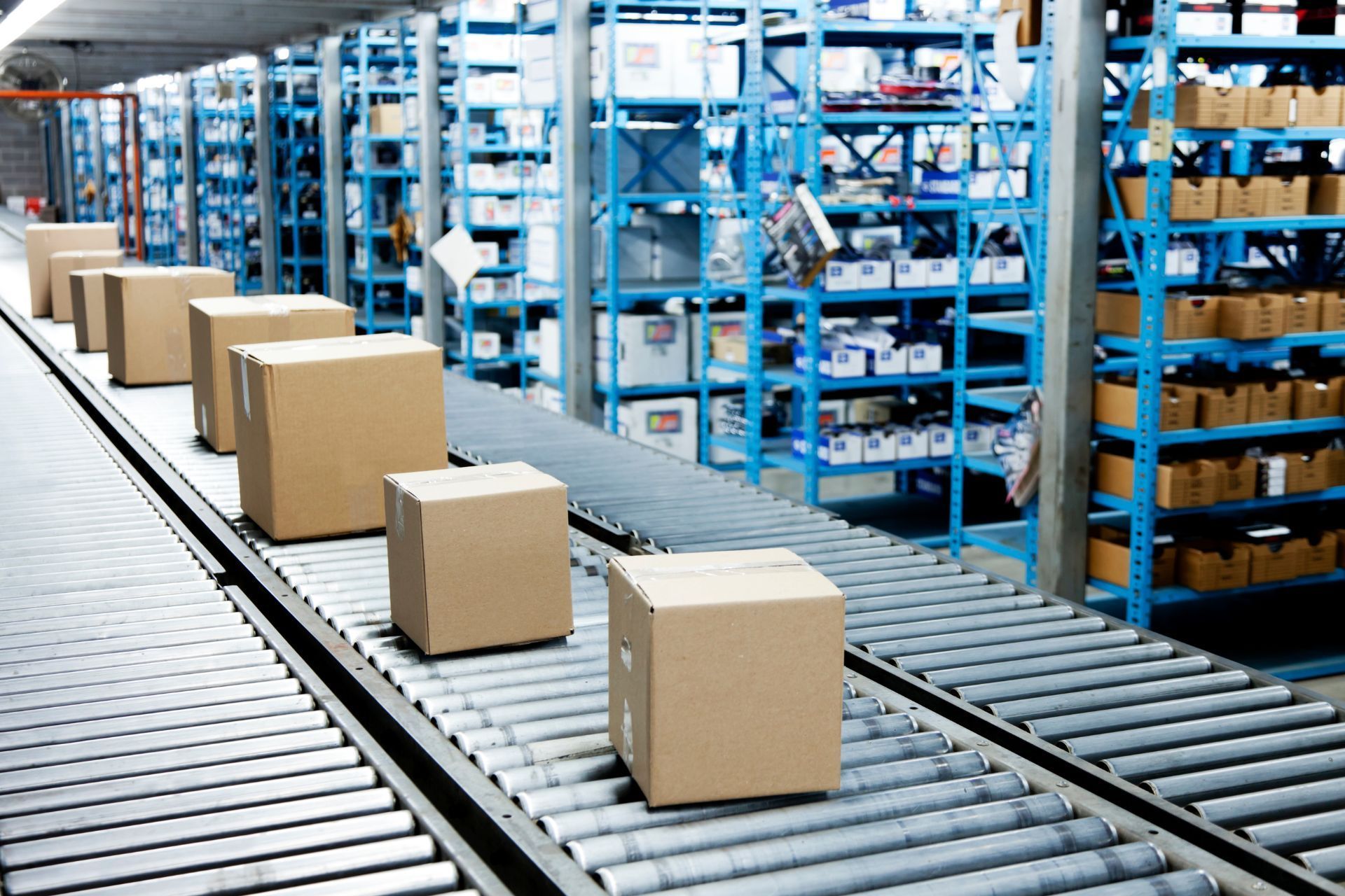 Cardboard boxes moving on rollers in a warehouse aisle with blue shelving racks