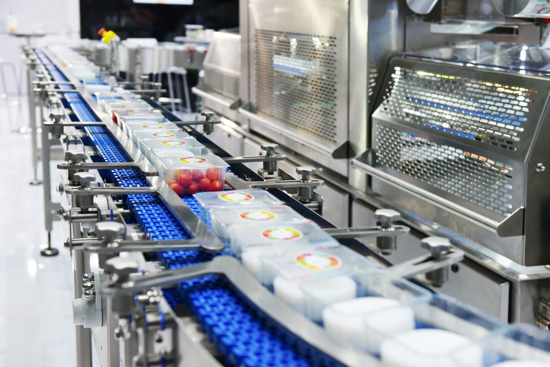 Automated factory conveyor line carrying white containers through stainless steel machinery