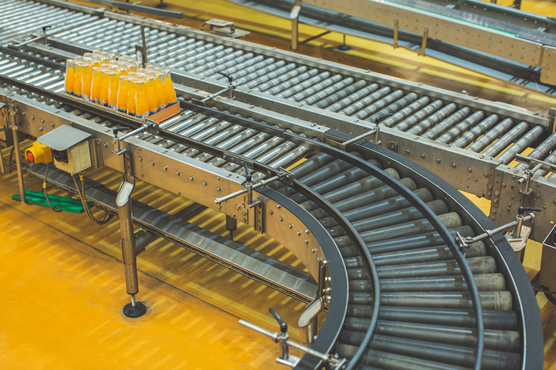 Curved conveyor belt transporting orange bottles in a factory assembly line