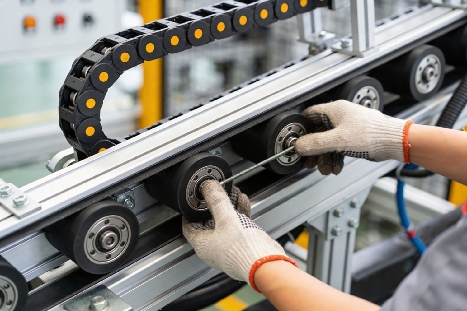 Gloved hands adjusting rollers on a metal conveyor system in a factory