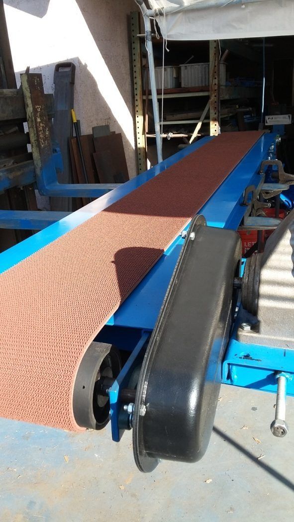 Brown belt conveyor moving material through a blue industrial machine area