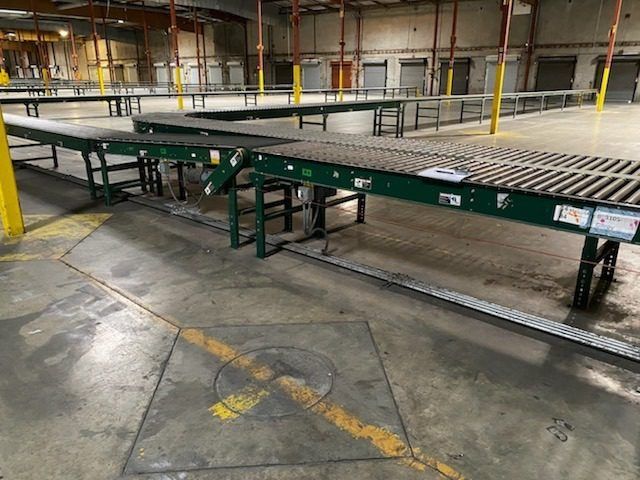 Warehouse interior with green conveyor belts on a concrete floor and yellow safety poles