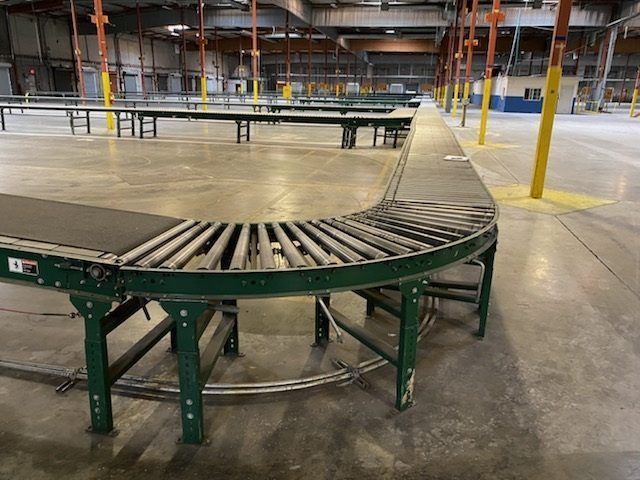 Curved metal conveyor belt in an empty warehouse with yellow support columns and concrete floor