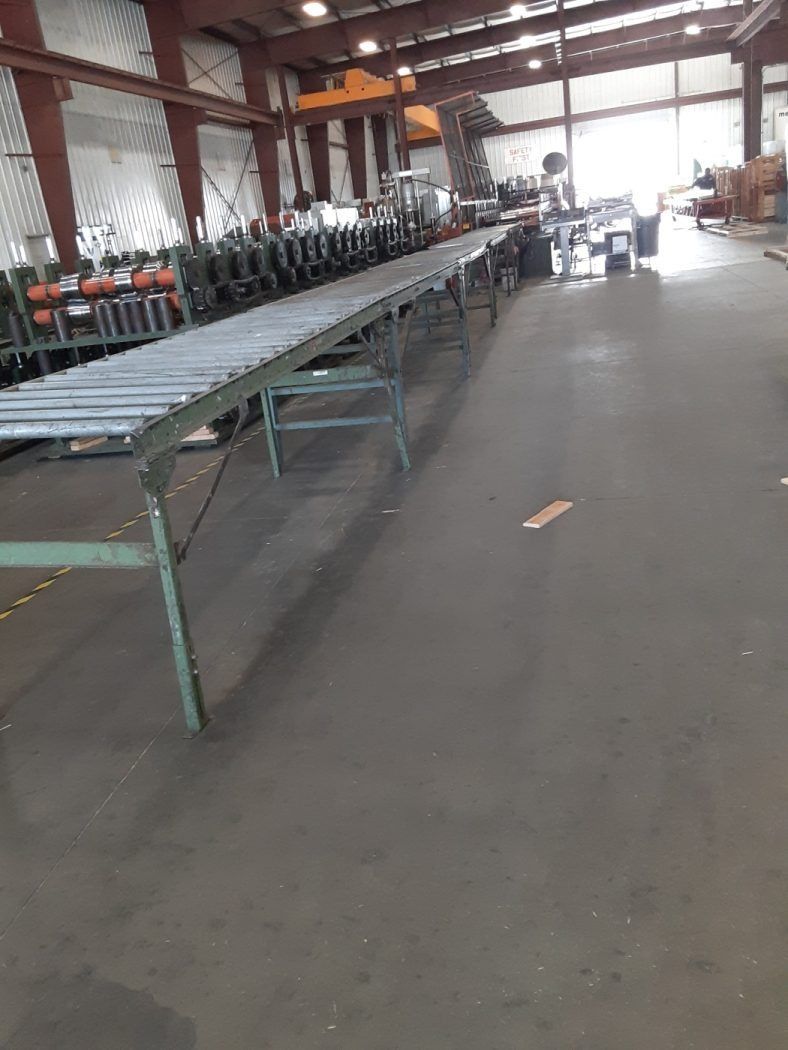 Industrial warehouse with long metal conveyor tables and machinery under a high red steel roof
