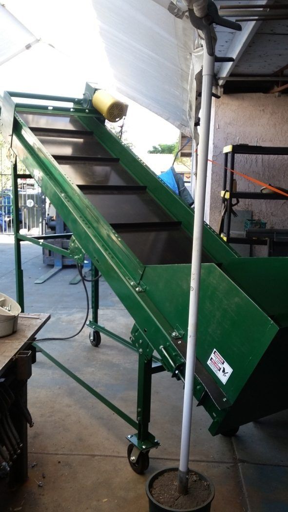 Green industrial conveyor with black steps in a workshop, beside a metal pole and machinery