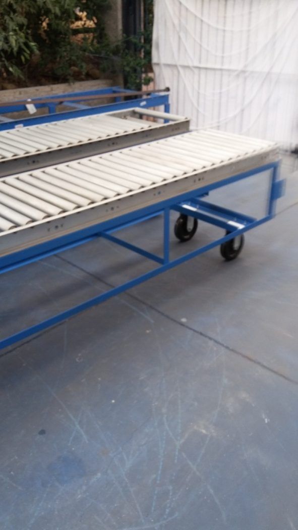 Blue metal conveyor table with white rollers and wheels in a workshop setting