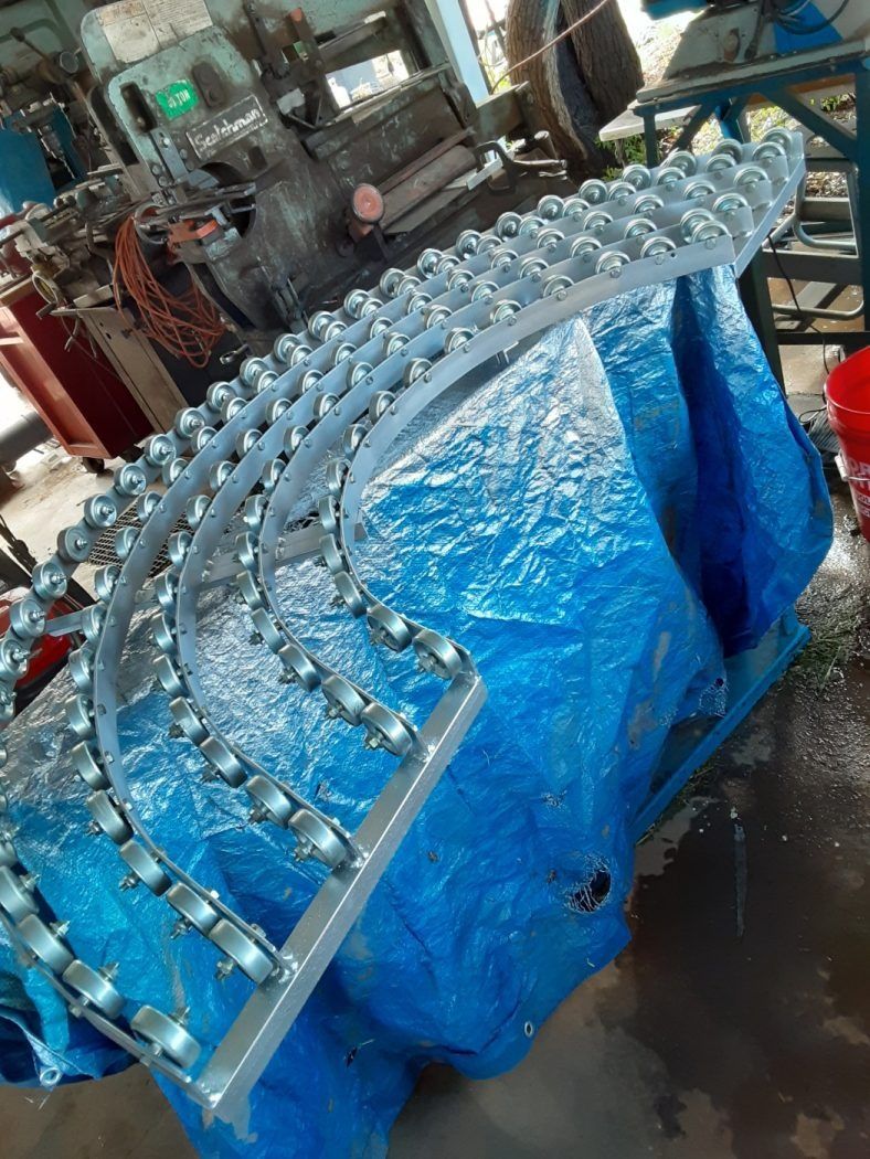 Curved rows of clear bottles on a metal conveyor, covered partly by a blue tarp in an industrial setting