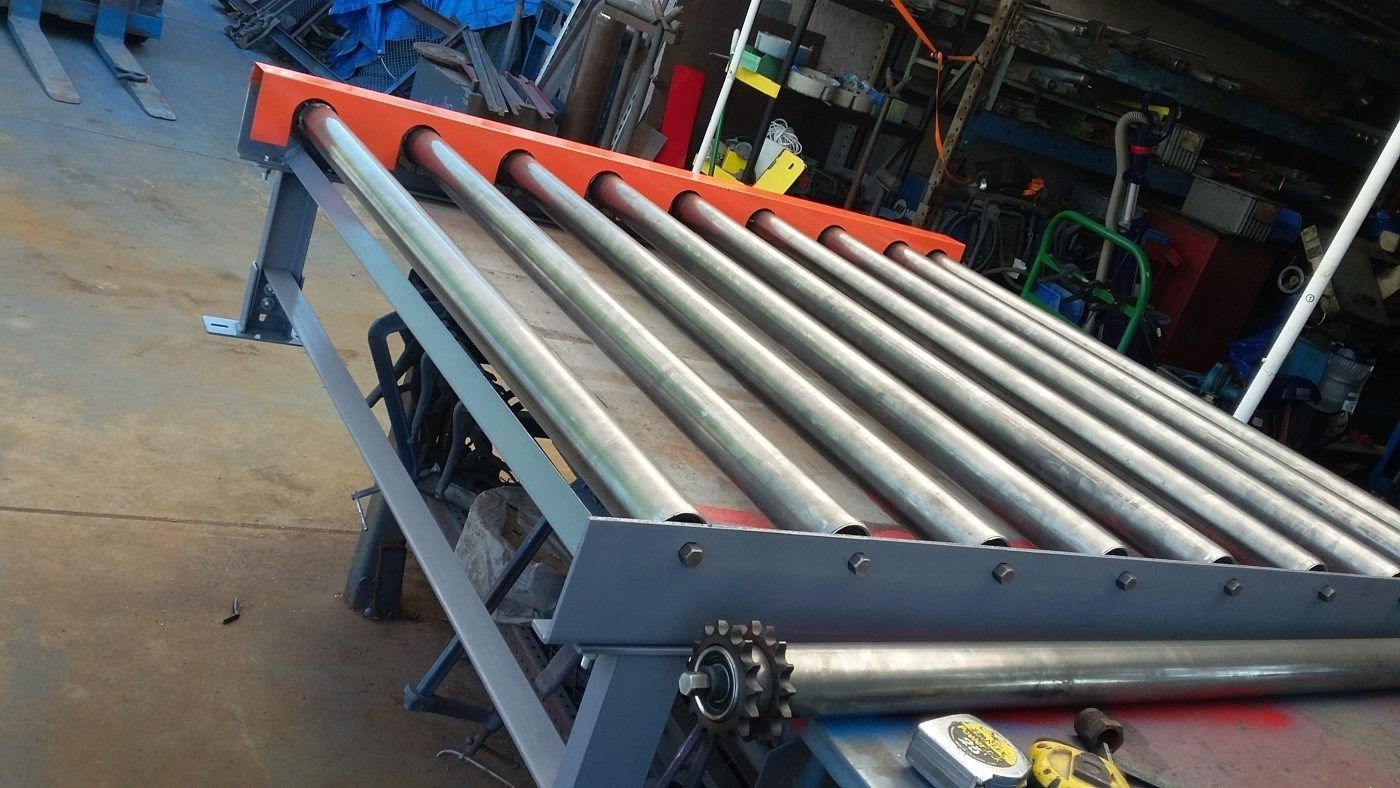 Factory conveyor with metal rollers and orange supports in an صنعتی workshop