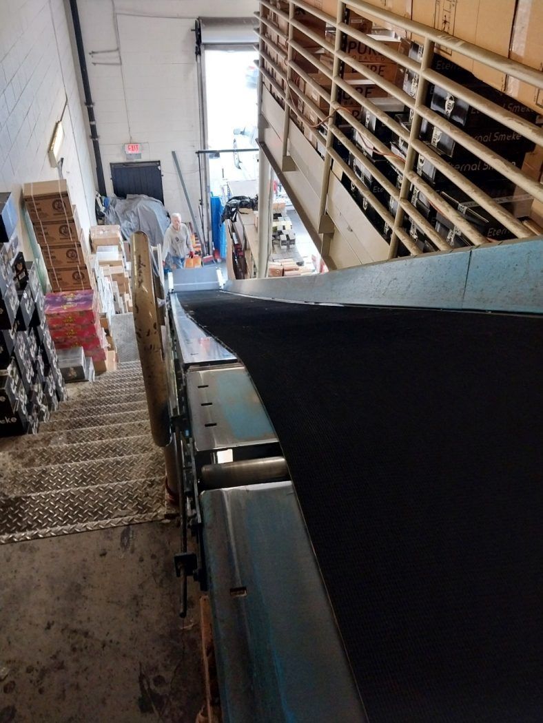 Narrow industrial walkway beside metal shelving and machinery, with a bright doorway at the far end.