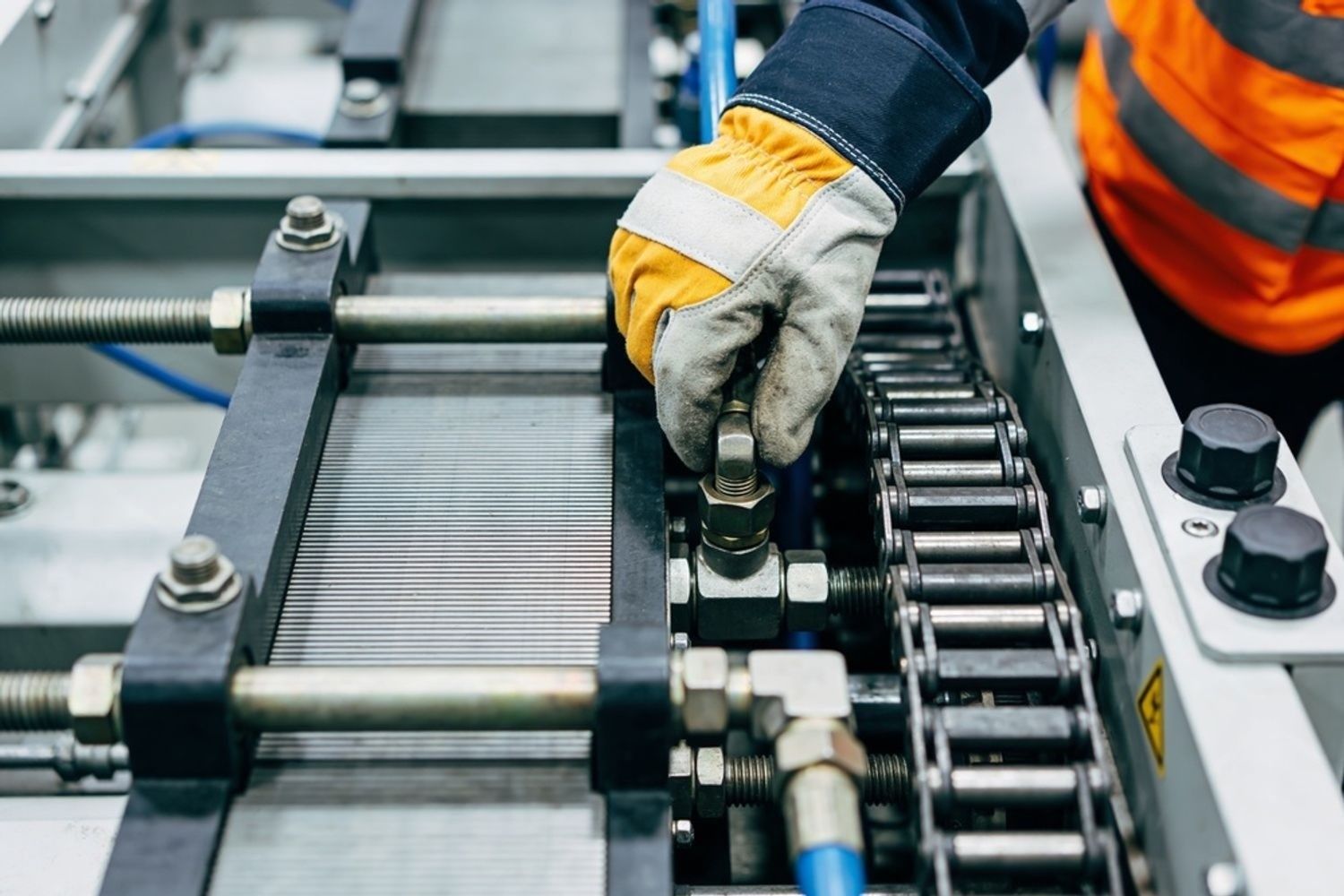 Gloved worker adjusting machinery on a conveyor line in an industrial setting