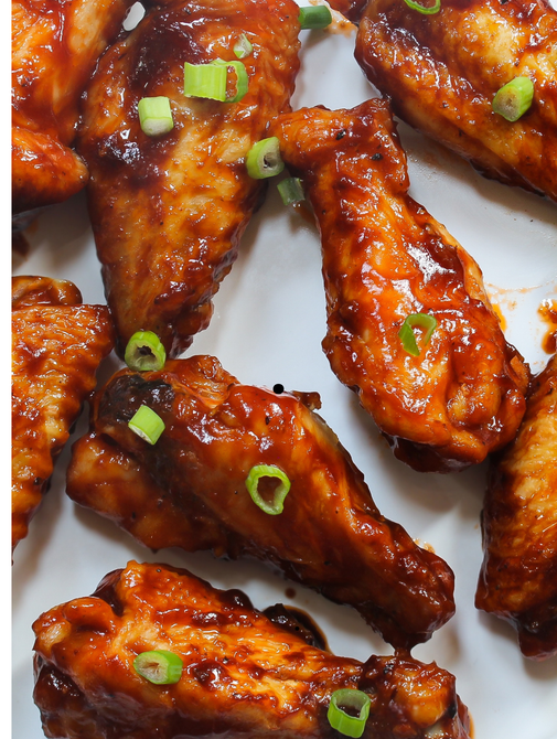 A white plate topped with chicken wings and green onions