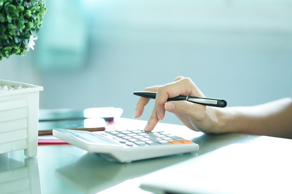 Hand Using Calculator & Holding Pen — Accountants & Bookkeepers in Southern Highlands