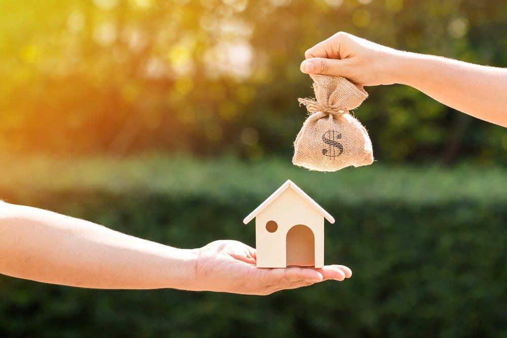Hand Exchanging Money Bag for House — Accountants & Bookkeepers in Southern Highlands