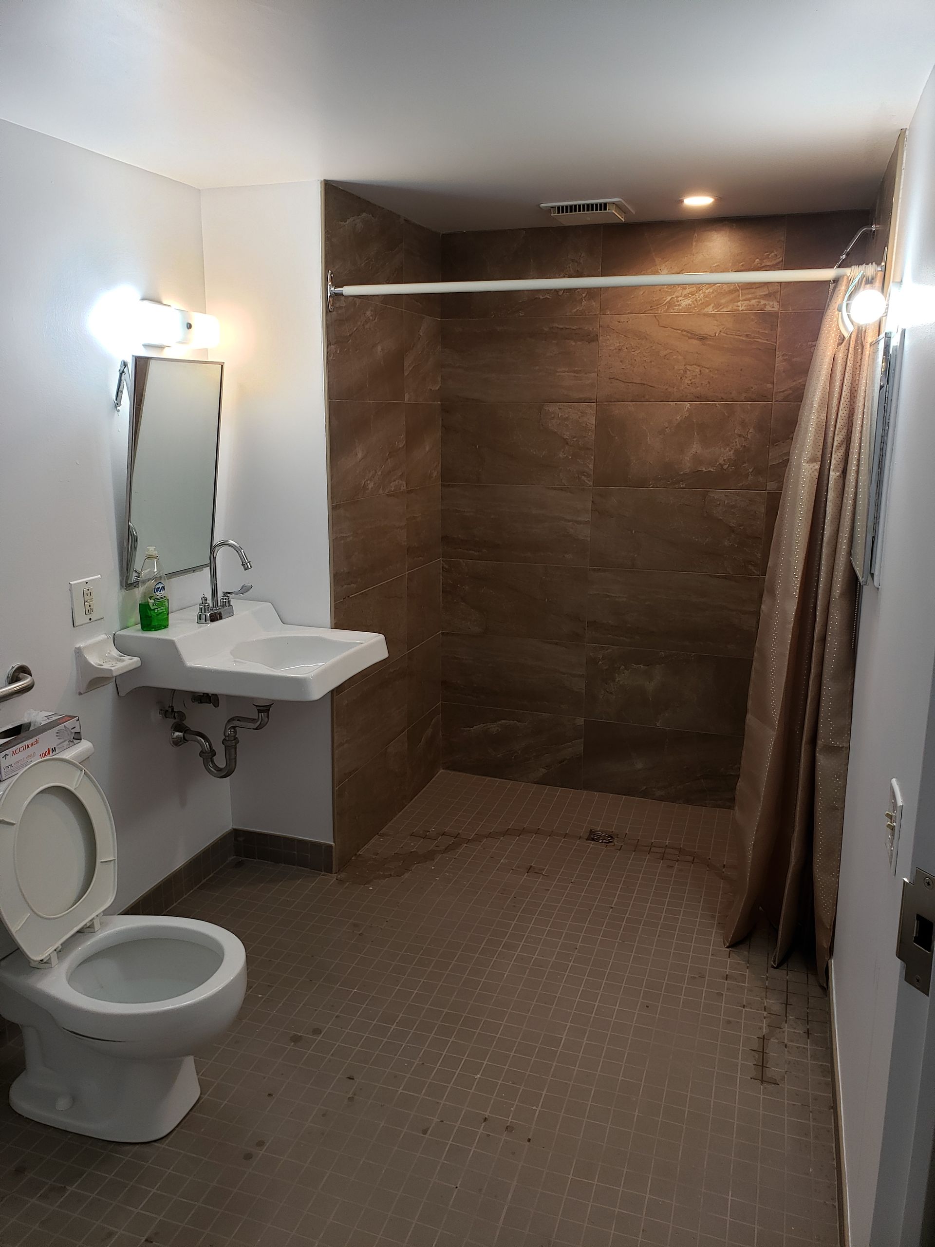 Salle de bains avec toilettes, lavabo et douche, avec un mur carrelé de brun.