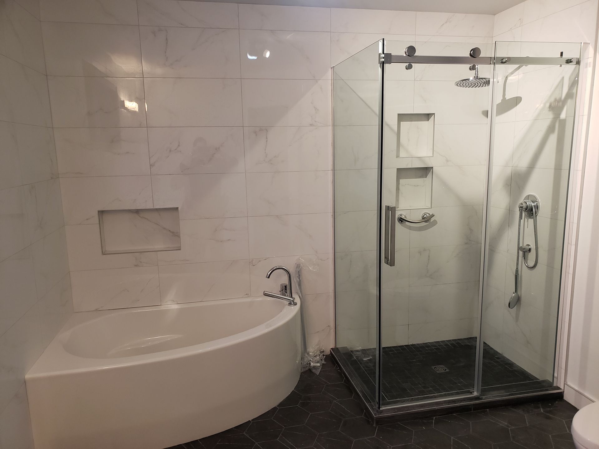 Salle de bains moderne avec baignoire d'angle, douche en verre et murs carrelés en marbre.