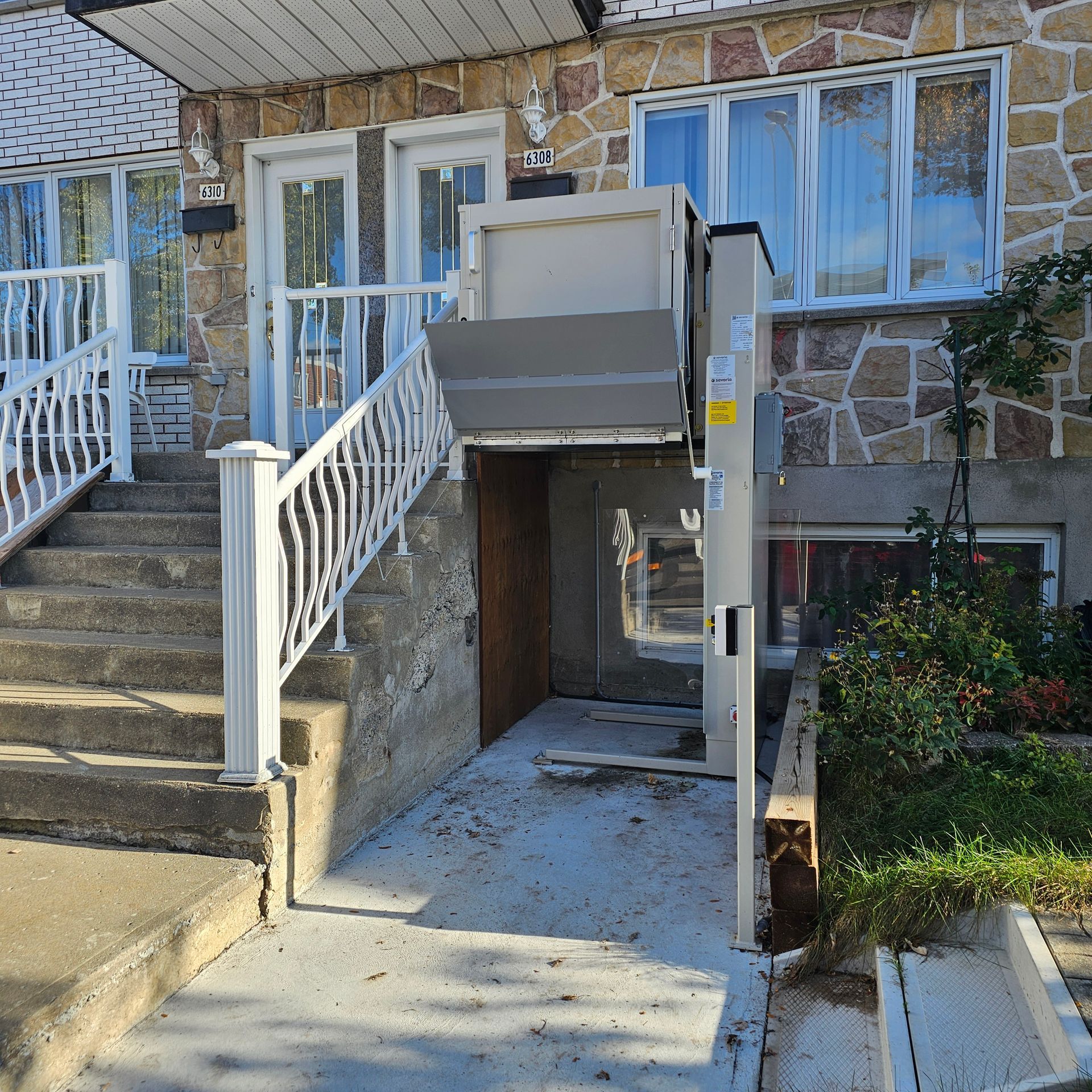Vue extérieure d'une maison équipée d'une plateforme élévatrice pour faciliter l'accès. Des marches en béton mènent à la porte d'entrée.