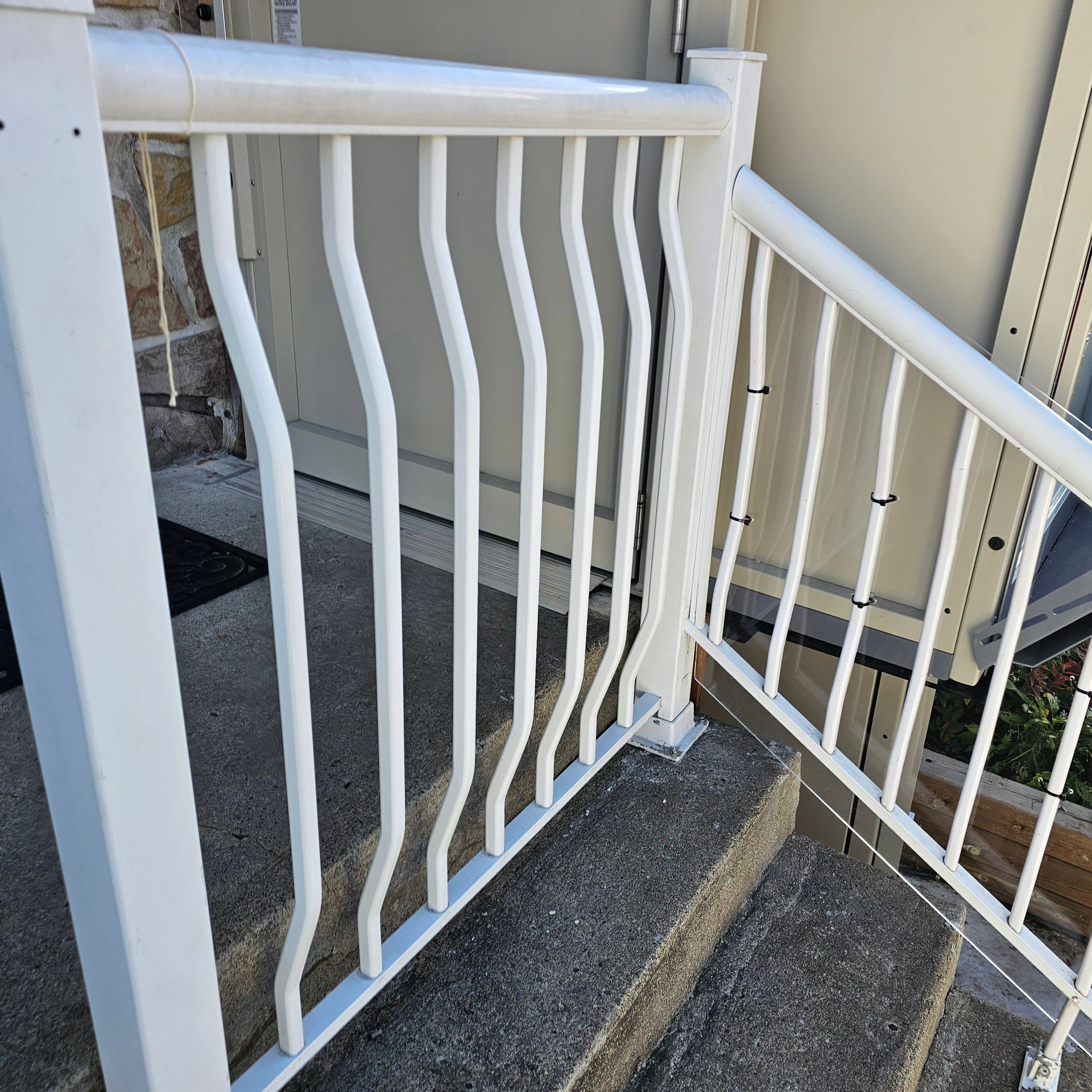 Rambarde en métal blanc avec barres verticales ondulées sur marches en béton, servant de main courante pour la sécurité.