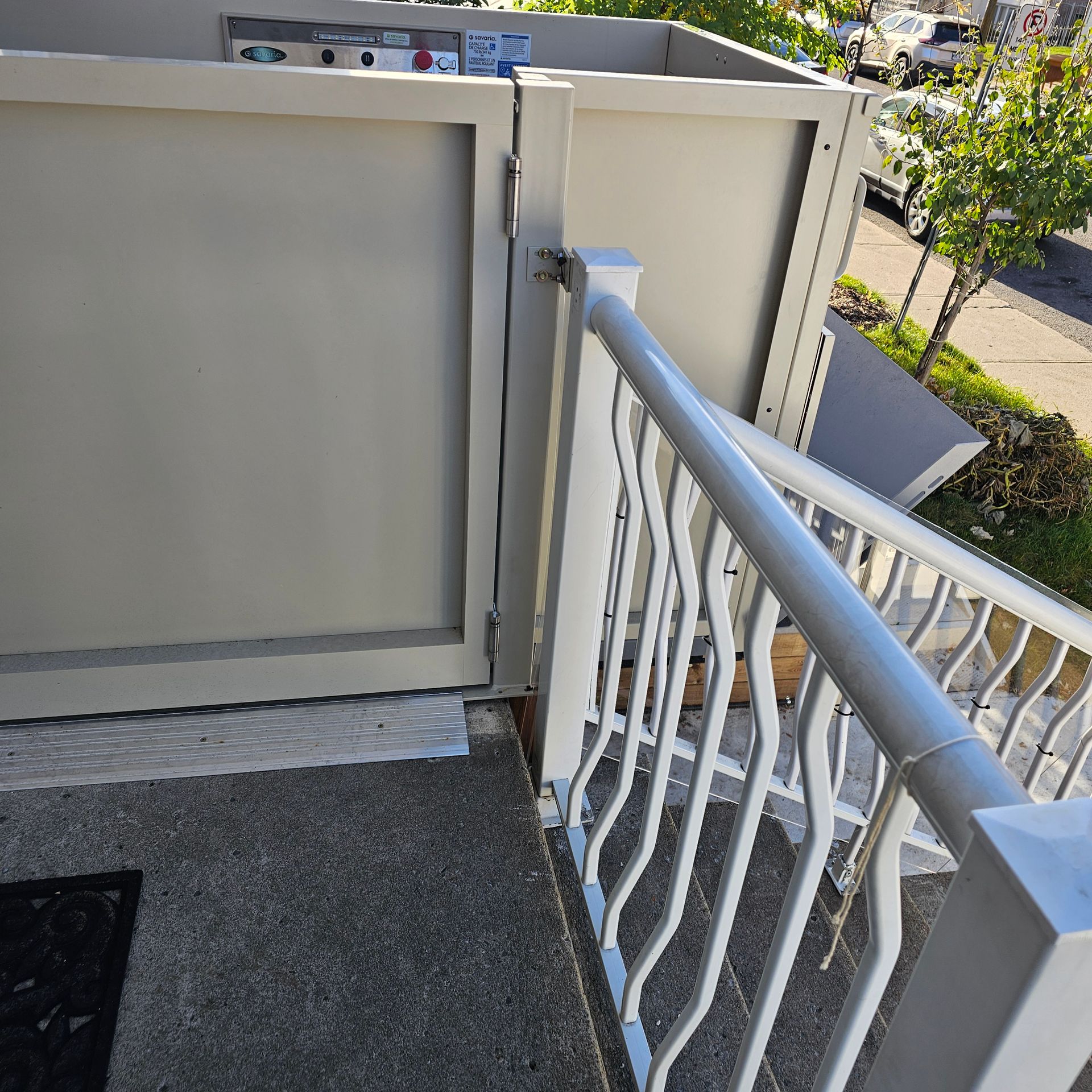 Balcon extérieur avec panneaux métalliques gris clair et rambarde blanche ; des marches en béton y mènent.