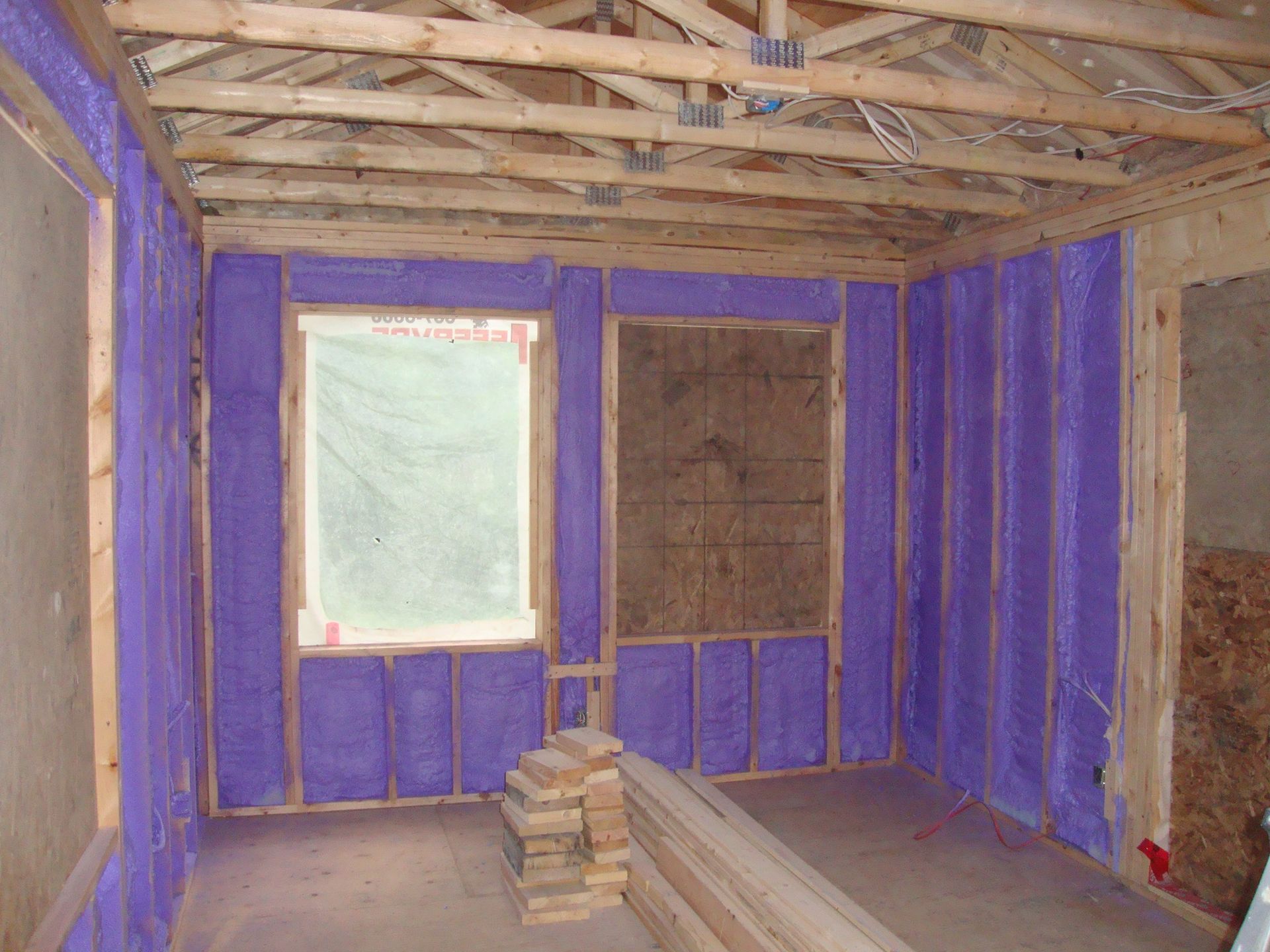 Intérieur d'une pièce en construction avec de l'isolant violet projeté entre les montants en bois.