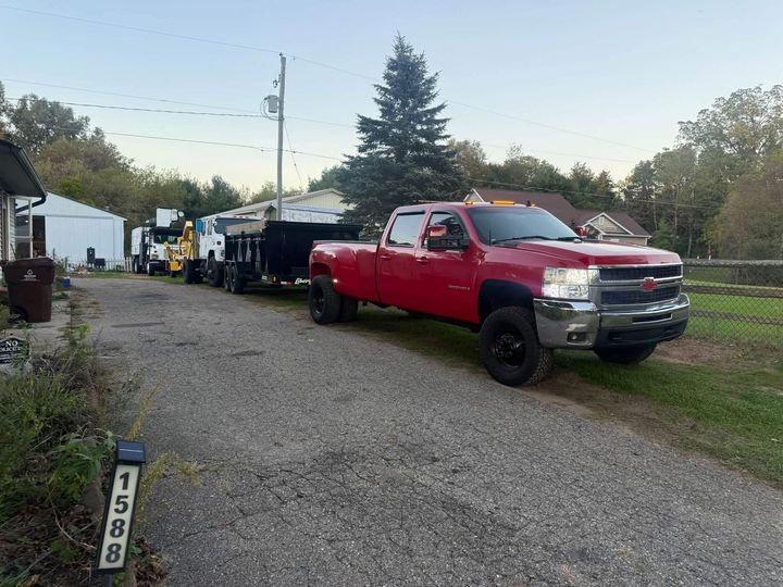 Red pickup truck towing a long black trailer on a gravel driveway beside a house at dusk