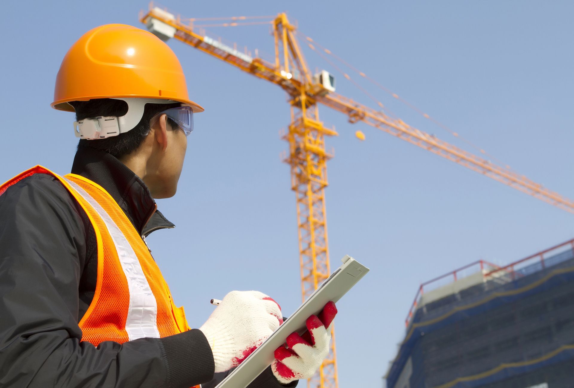 Operaio edile che indossa un casco e un giubbotto di sicurezza e osserva un cantiere con una gru.
