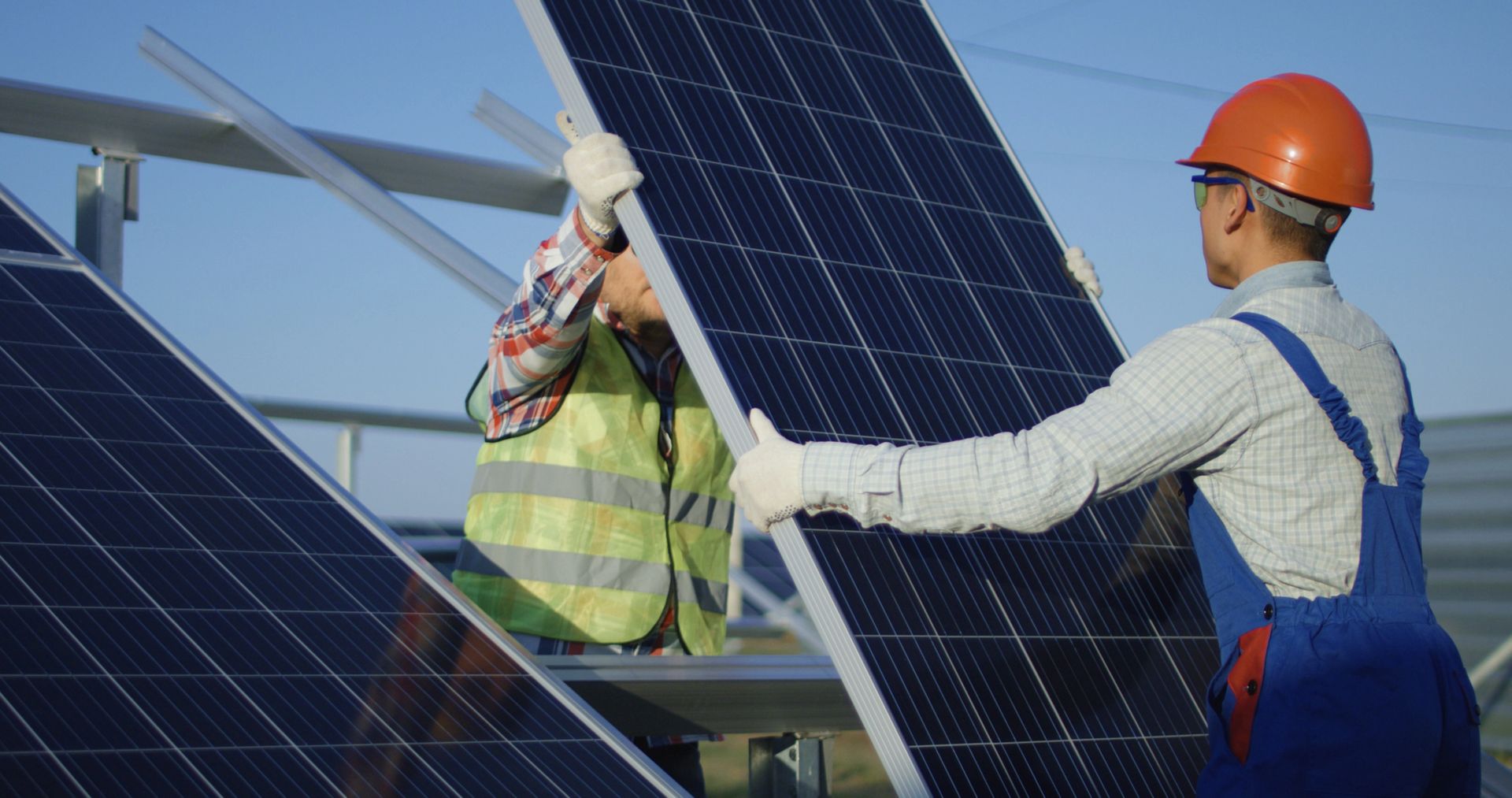 Operai che installano un pannello solare su un tetto; uno indossa un casco e una tuta blu.