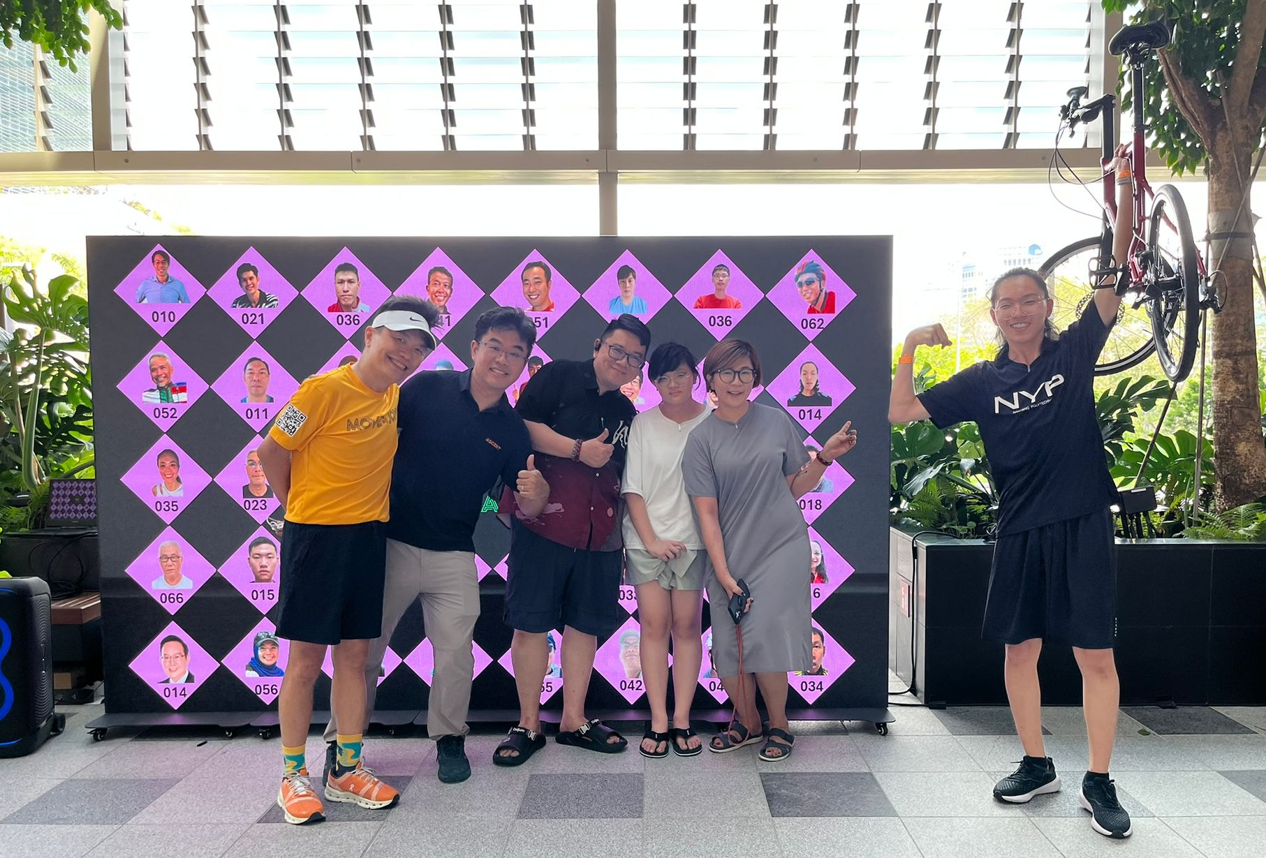 Group posing in front of a pink patterned backdrop, with one person waving beside them