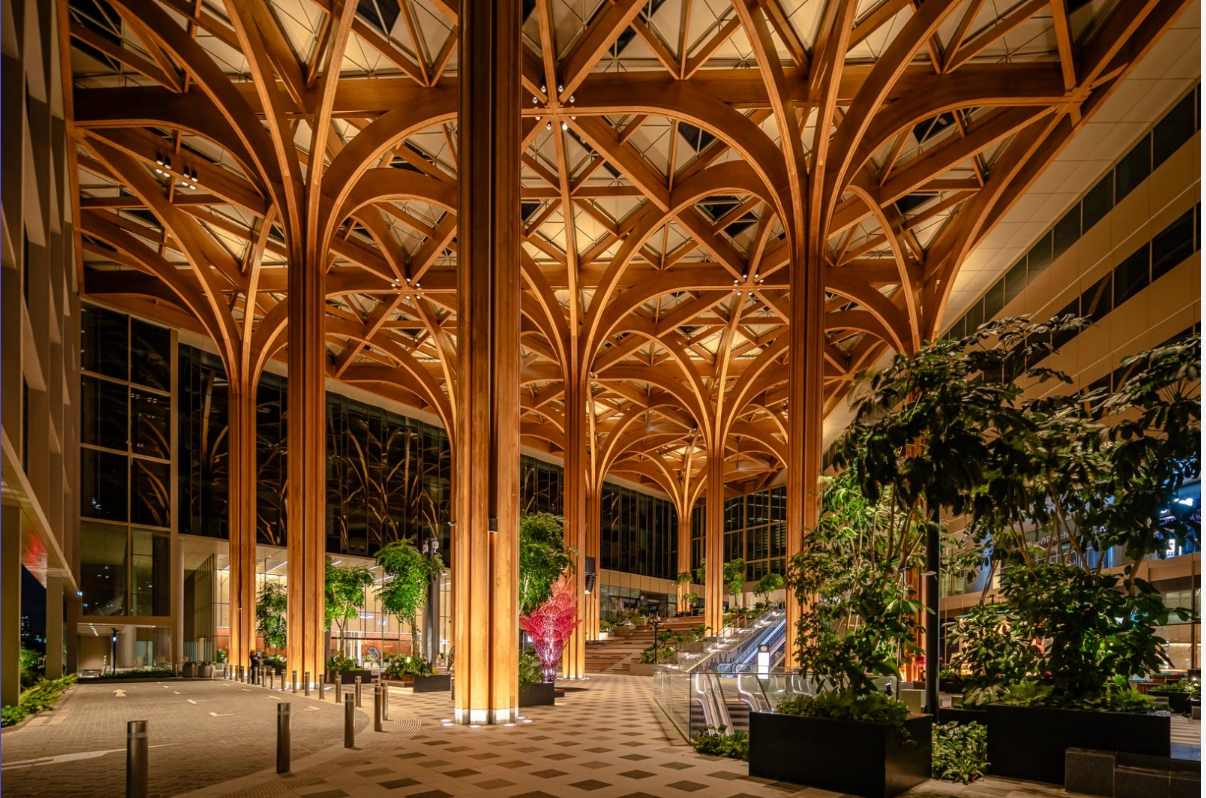 Indoor courtyard with tall wooden arches, warm lighting, and trees at night