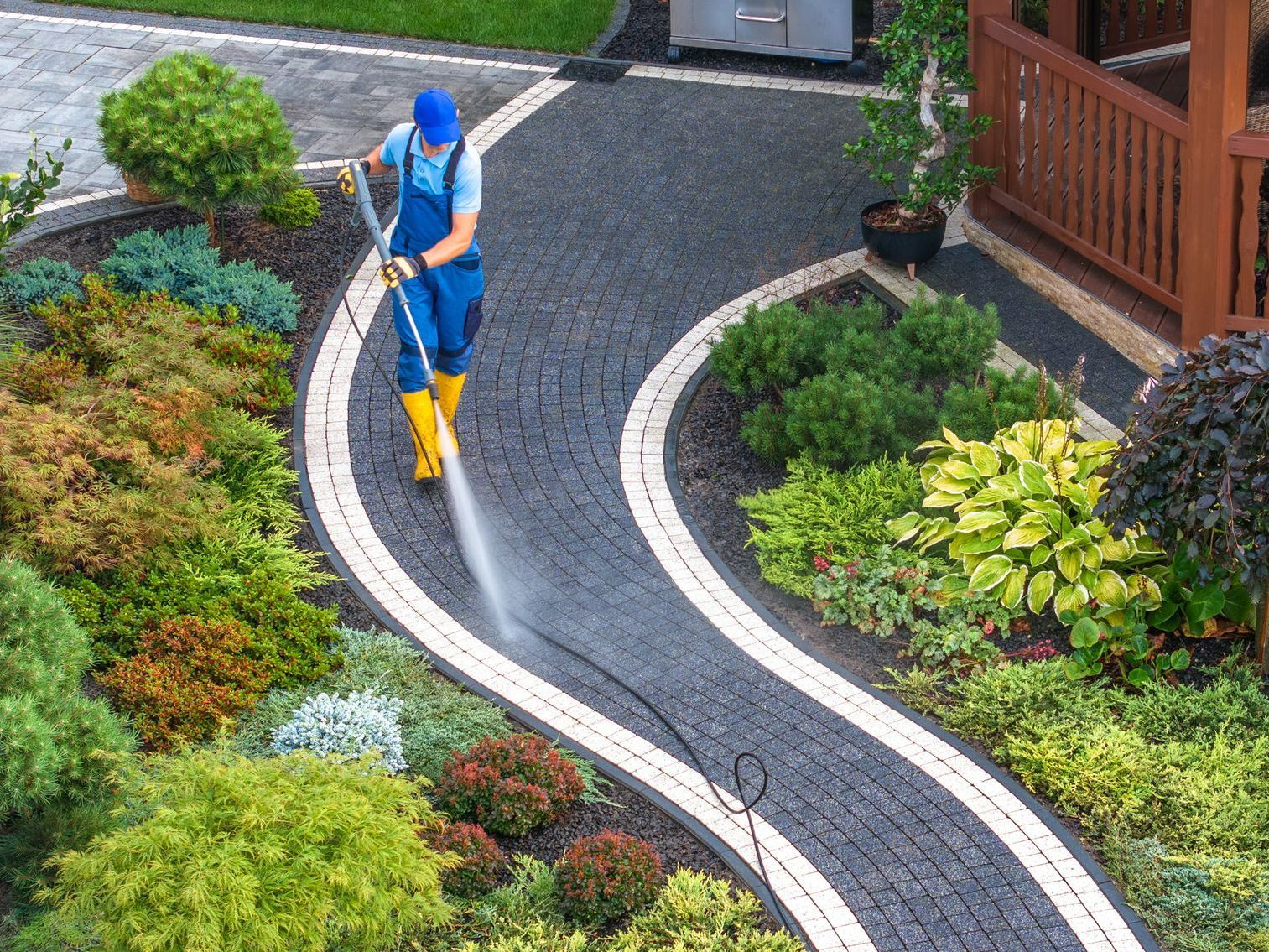 A man uses a high-pressure washer to clean a walkway in a garden. A man uses a high-pressure washer to clean a walkway in a garden.