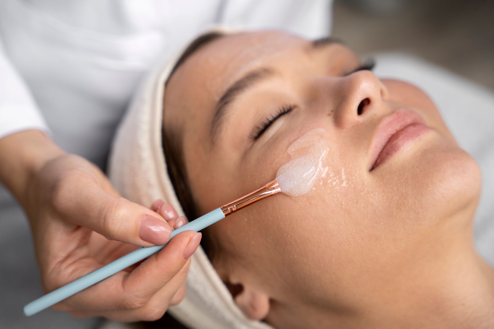 Spa therapist applying facial cream with a brush to a client’s face