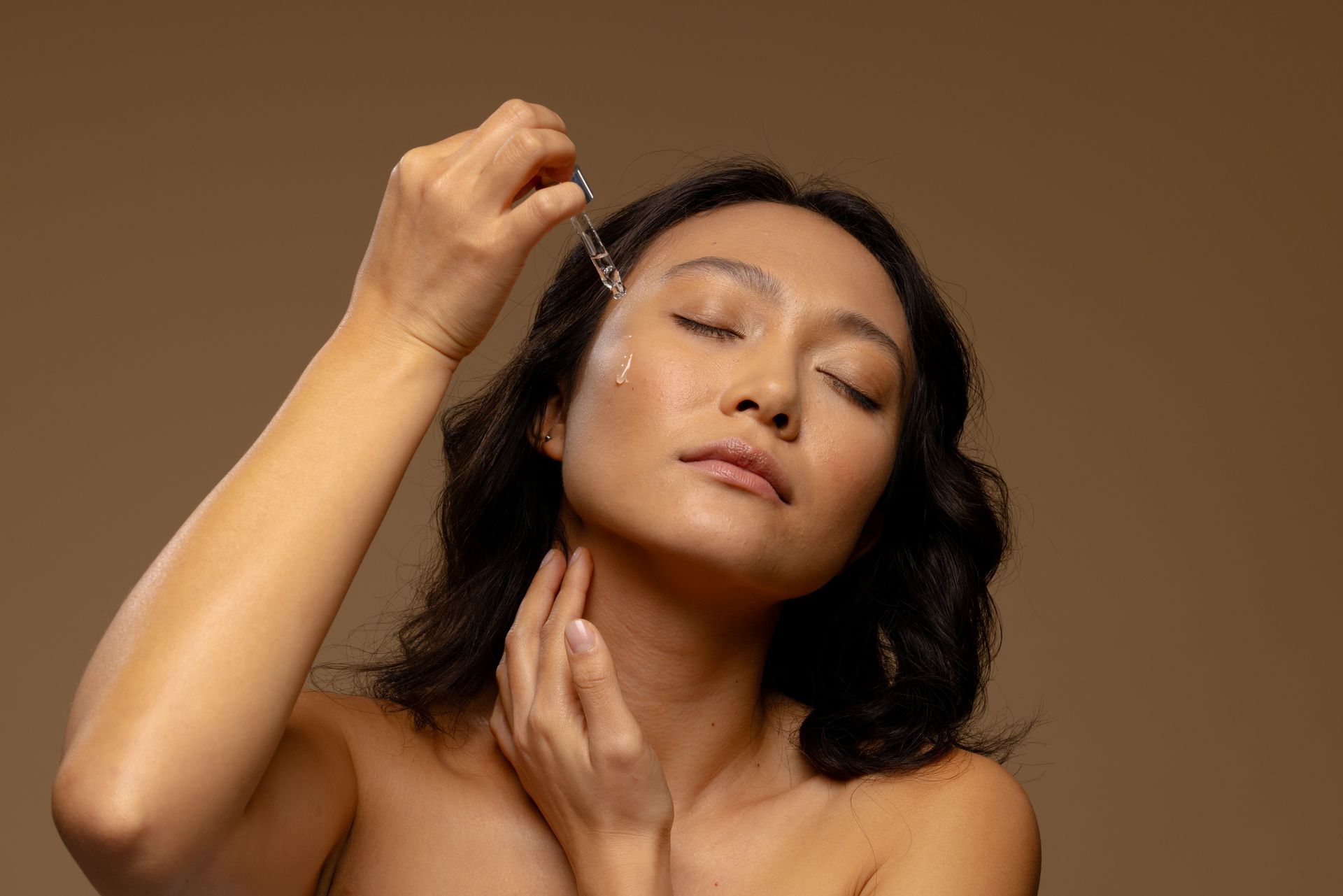 Woman applying makeup with a brush against a brown background