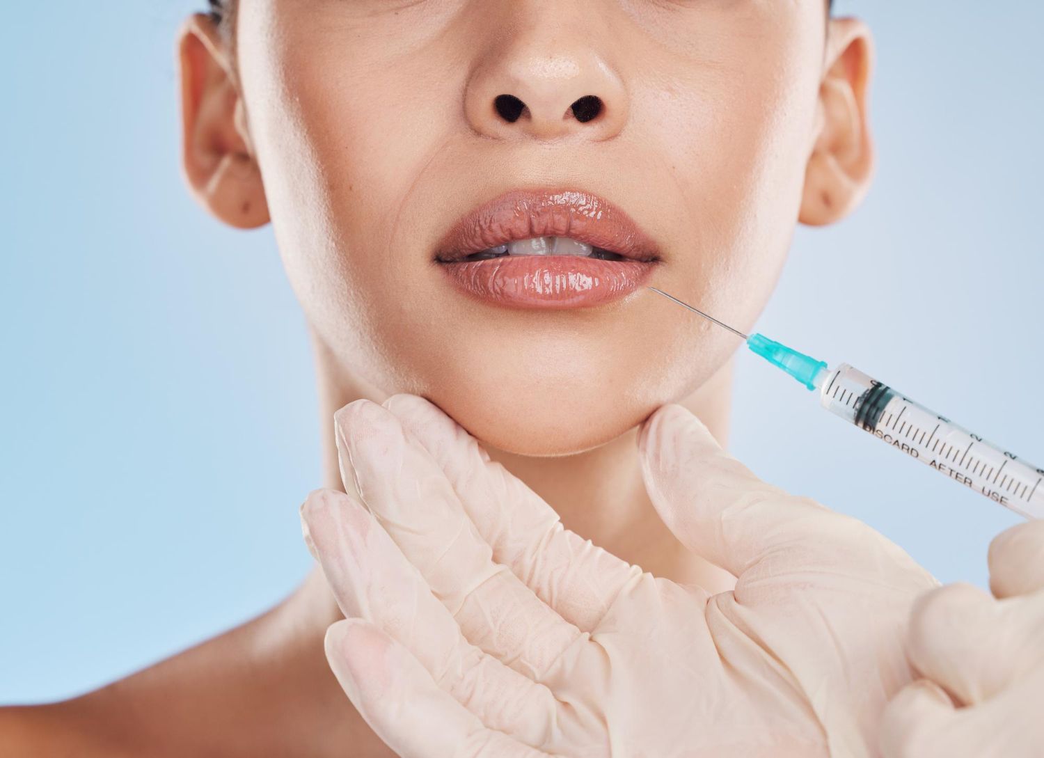 A person receives a cosmetic lip filler injection from a practitioner wearing white medical gloves.
